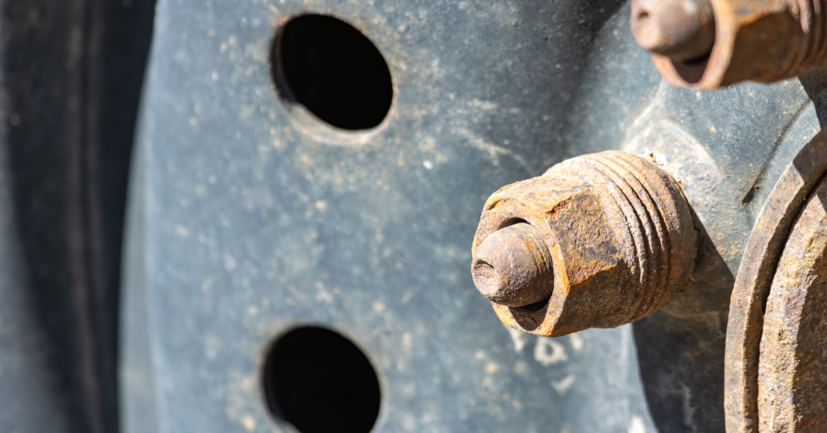 Bright sunlight shining on a car wheel with two rusty lug nuts attached to it. The wheel has some rust on the surface.