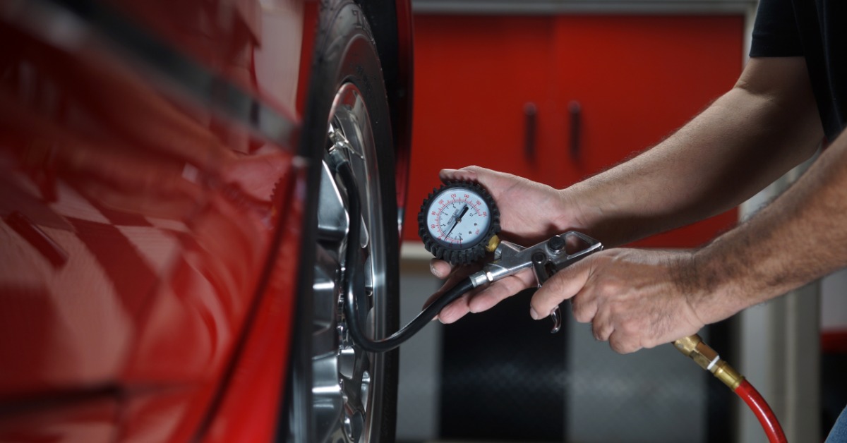 A close-up of a man holding up a tire pressure inflation gauge to the valve stem of the tire of a red car.