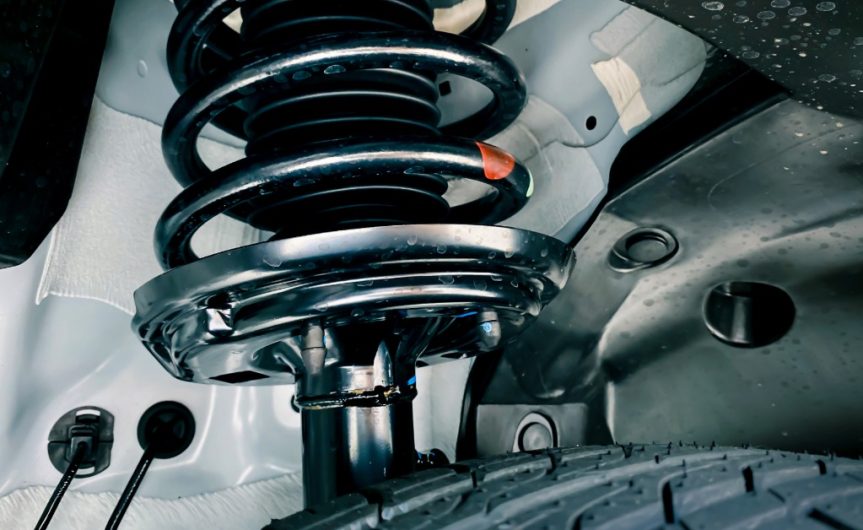 Modern shock absorbers and a spring suspension system on a car. The suspension parts are lightly covered in dried mud.