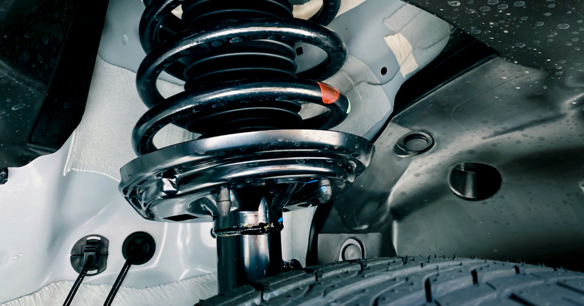 Modern shock absorbers and a spring suspension system on a car. The suspension parts are lightly covered in dried mud.