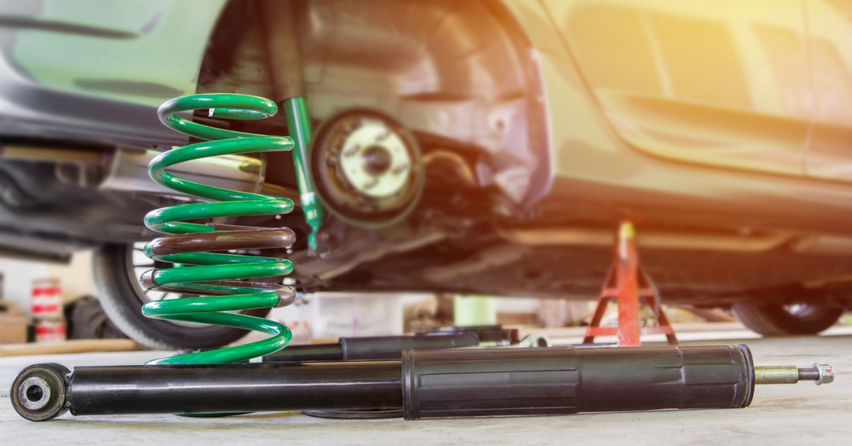 A green coil spring and black shock absorber on the ground next to a vehicle missing its rear passenger-side tire.