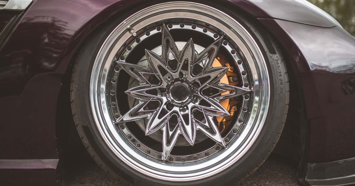 A close-up of the custom wheel and tire of a purple sports car. The wheel features an intricate starburst design.