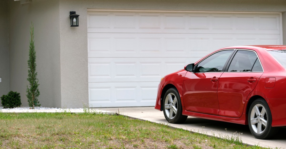 A small red car parked in the driveway of a beige house with a wide, white garage during the daytime.