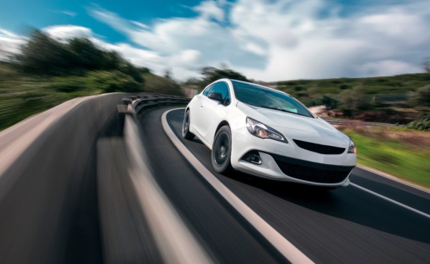 An action shot of the front of a white four-door sedan taking a corner of a mountain road at high speed.