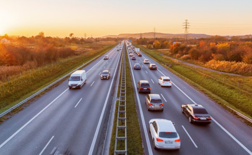 Many cars driving on the highway on a sunny day. One lane has heavy traffic, and the other does not.