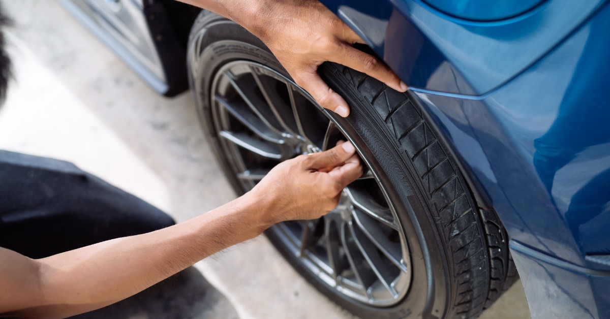 An overhead close-up of a person using their fingers to remove the cap of a tire valve stem from a blue car's tire.