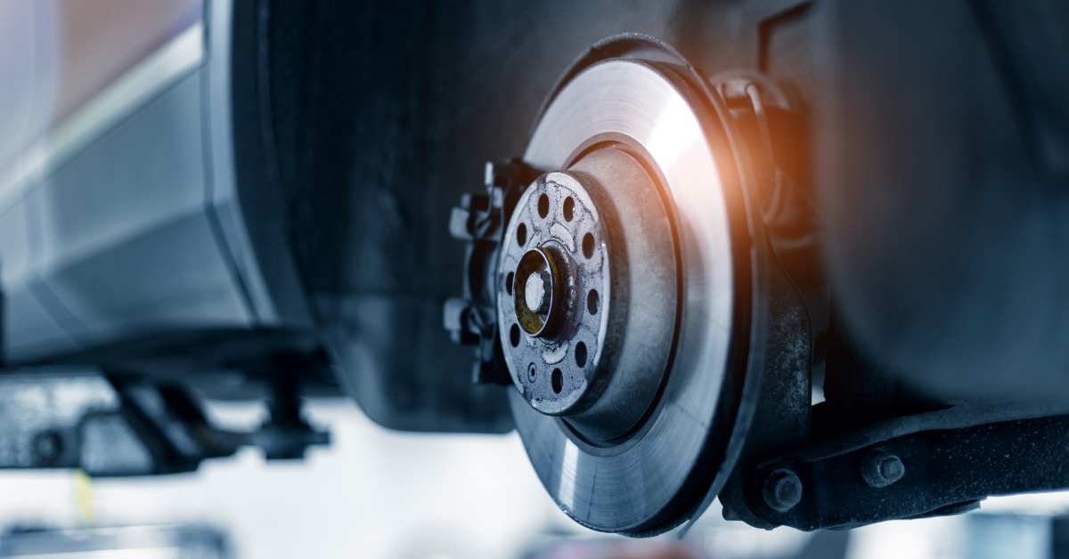 A silver steel brake rotor and wheel hub exposed inside a car's wheel well, with the tire removed in a workshop.
