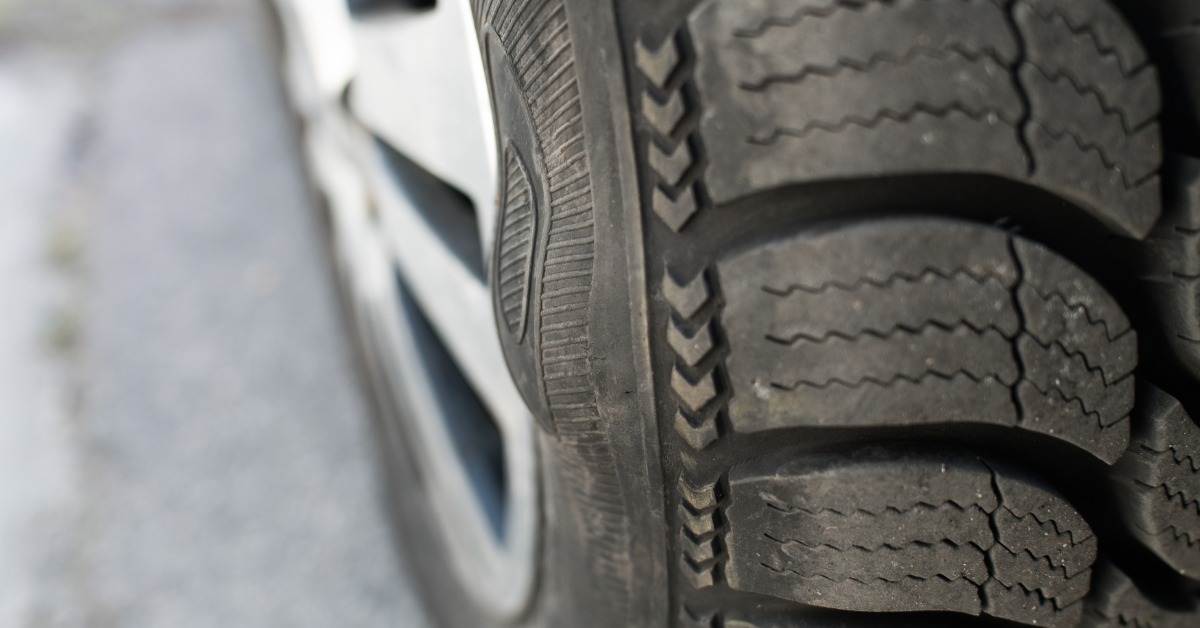 A close-up of a car tire and wheel with the sidewall containing a bubble indicating internal structural failure.