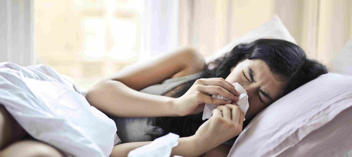 Mujer recostada en una cama con gripa o resfriado.