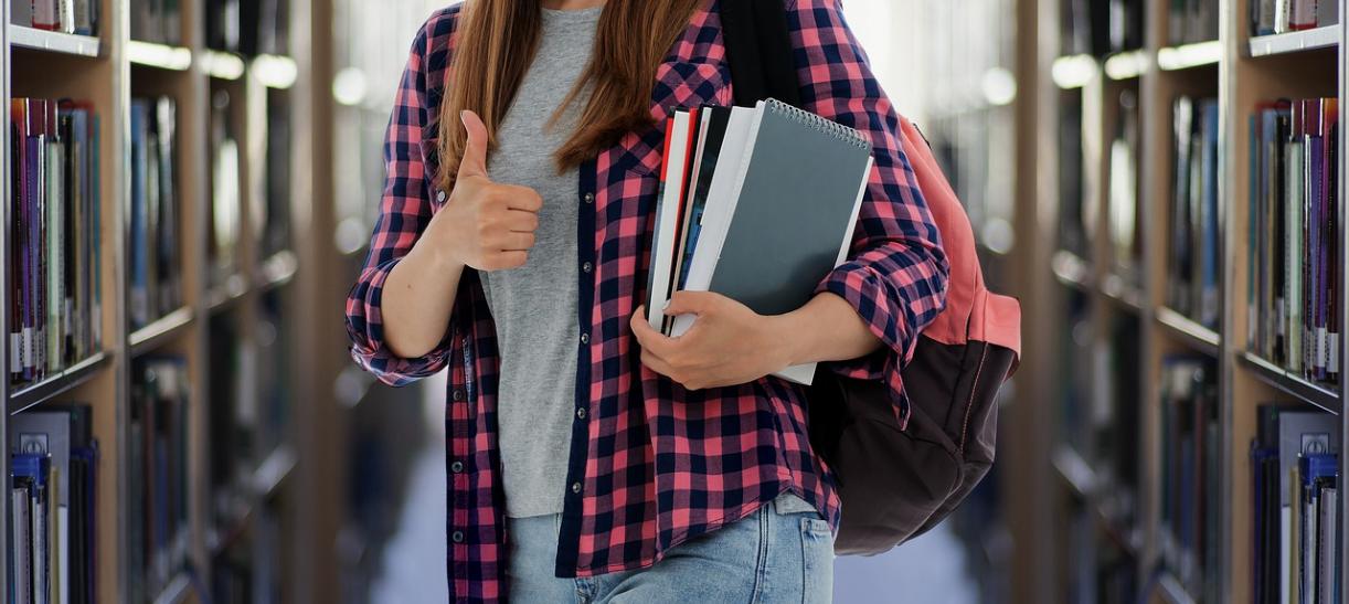 Foto de una estudiante cargando libros en la biblioteca de una universidad