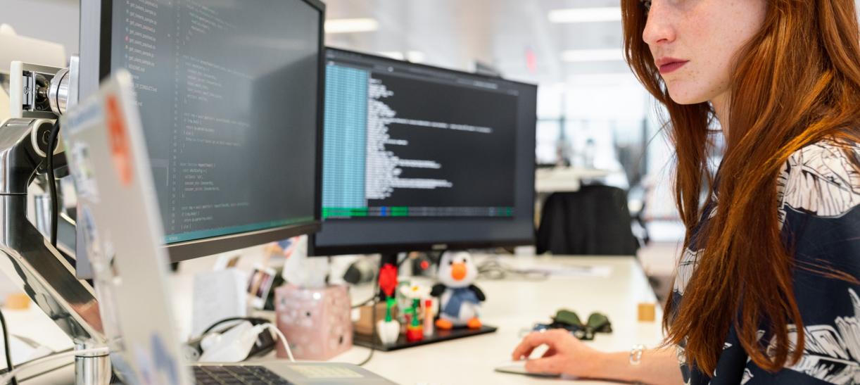 Foto de una mujer trabajando frente a varias pantallas de computador.