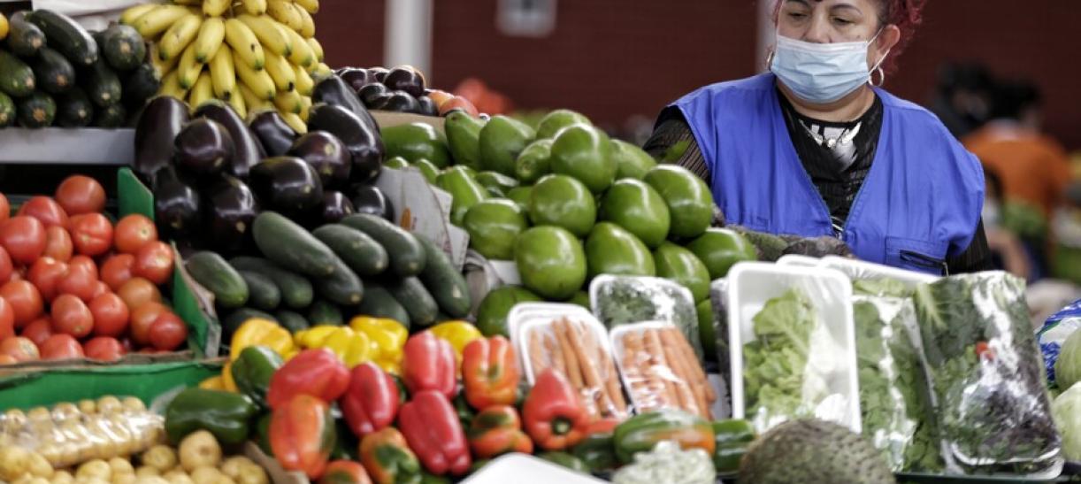 Foto de una comerciante frente a su puesto de verduras en una plaza de mercado.