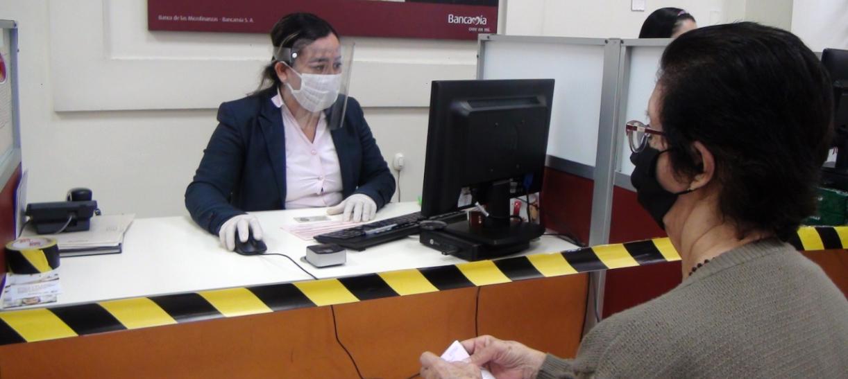 Imagen de una mujer adulta mayor siendo atendida por la funcionaria de un banco.
