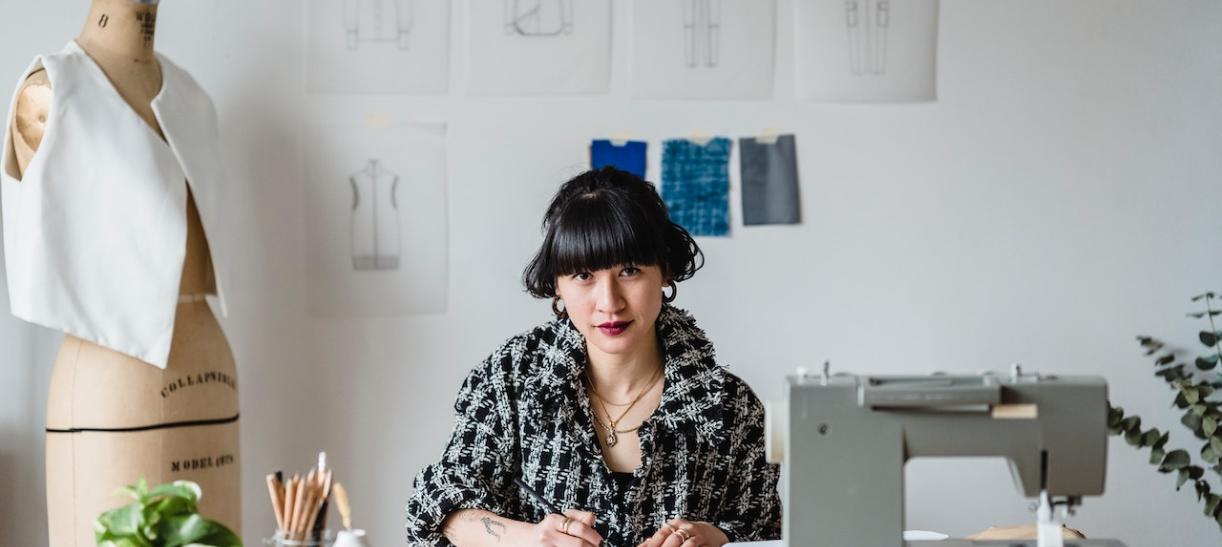 Mujer diseñadora en una mesa con máquina de coser. Ilustra nota sobre Fondo Emprender SENA.