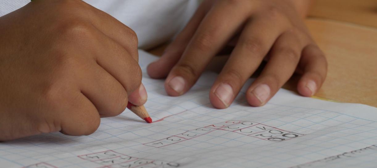 Manos de niño estudiante con lapiz y sobre un cuaderno.