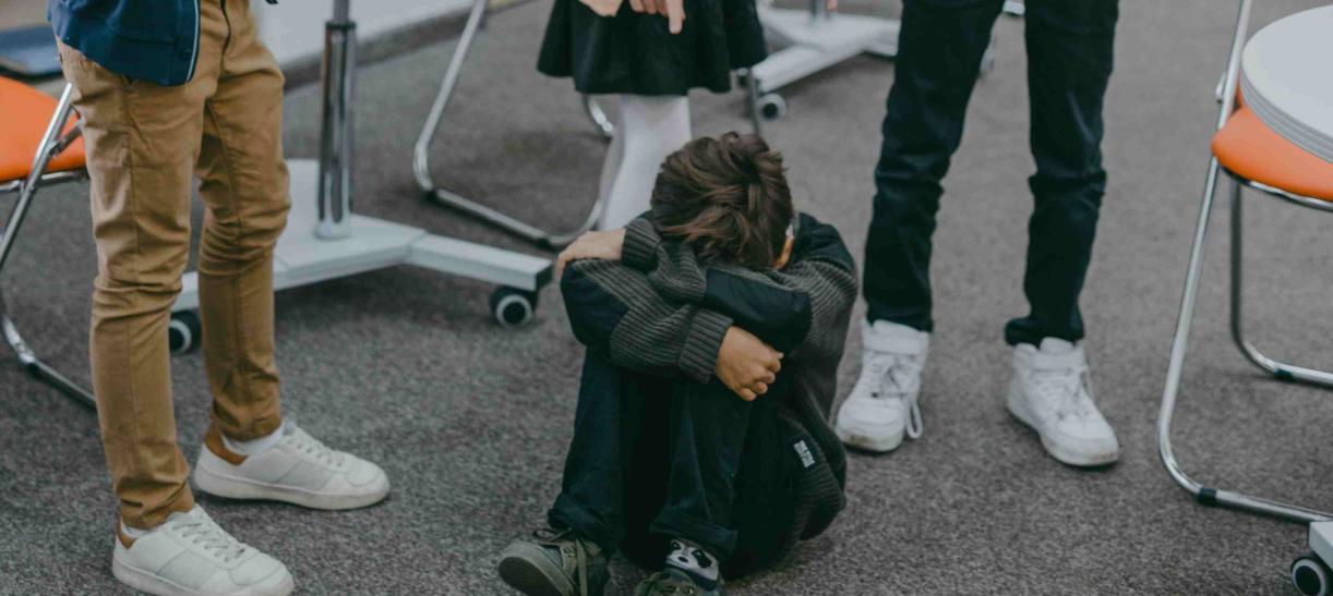 Niño se cubre la cara con sus brazos mientras otros niños lo señalan.