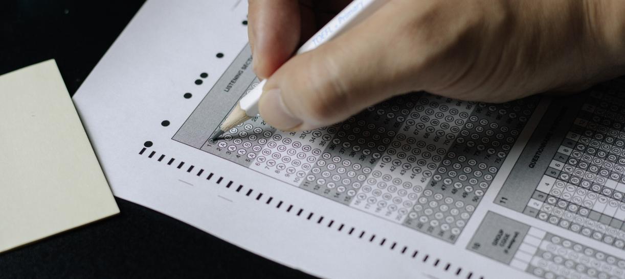 Mano de persona con lápiz marcando respuesta en formulario de prueba o examen.