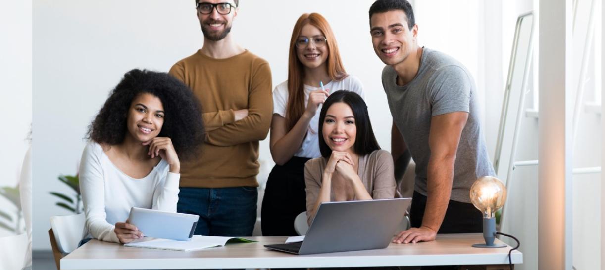 Tres mujeres y dos hombres jóvenes en oficina. Ilustra nota de prácticas con Estado Joven.