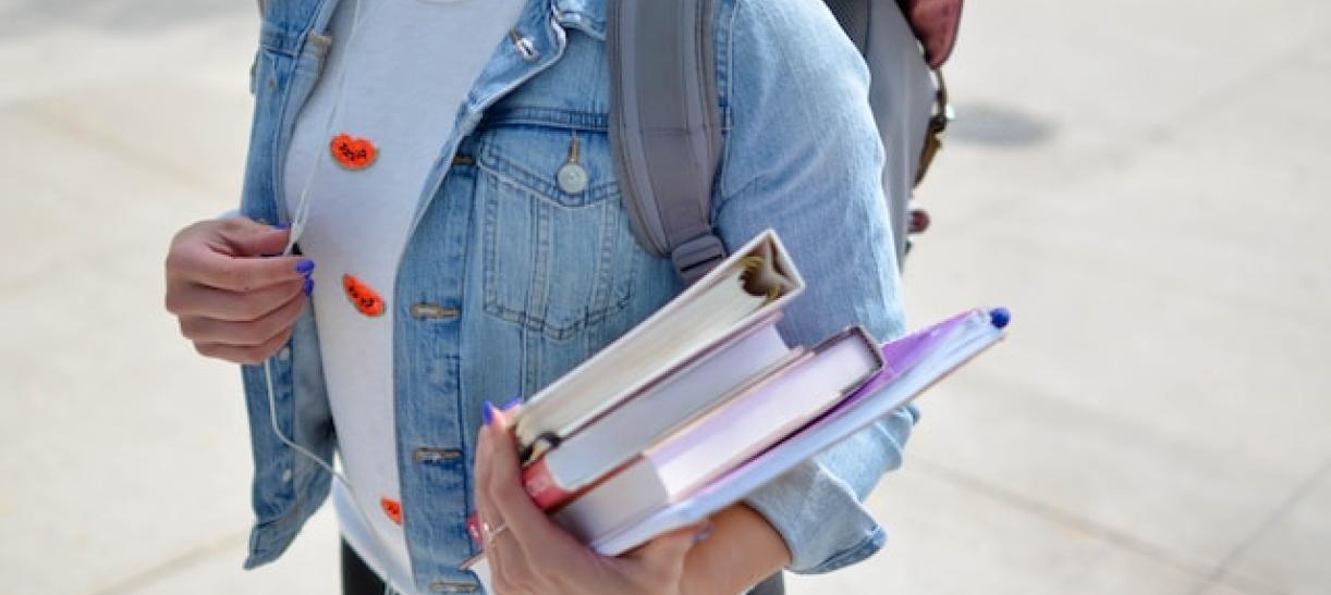 Joven mujer con libros en sus brazos. Ilustra nota sobre Matrícula Cero.