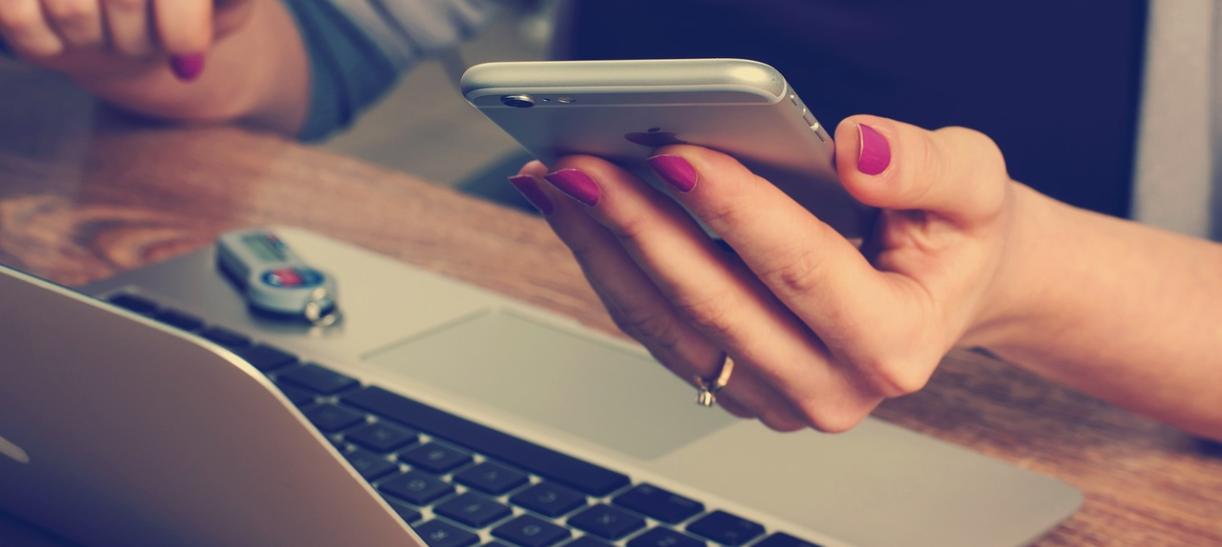 Manos de mujer sostienen un celular frente a una laptop. Ilustra nota sobre declaración de renta 'online'.
