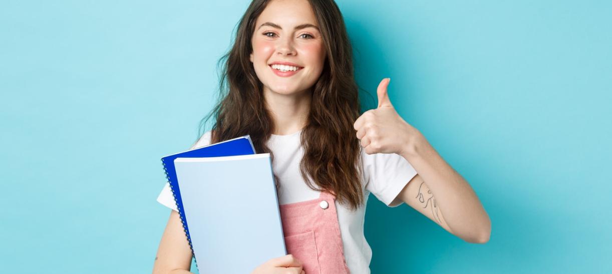 Joven con libros levantando el pulgar. Ilustra nota de condonación de créditos ICETEX.