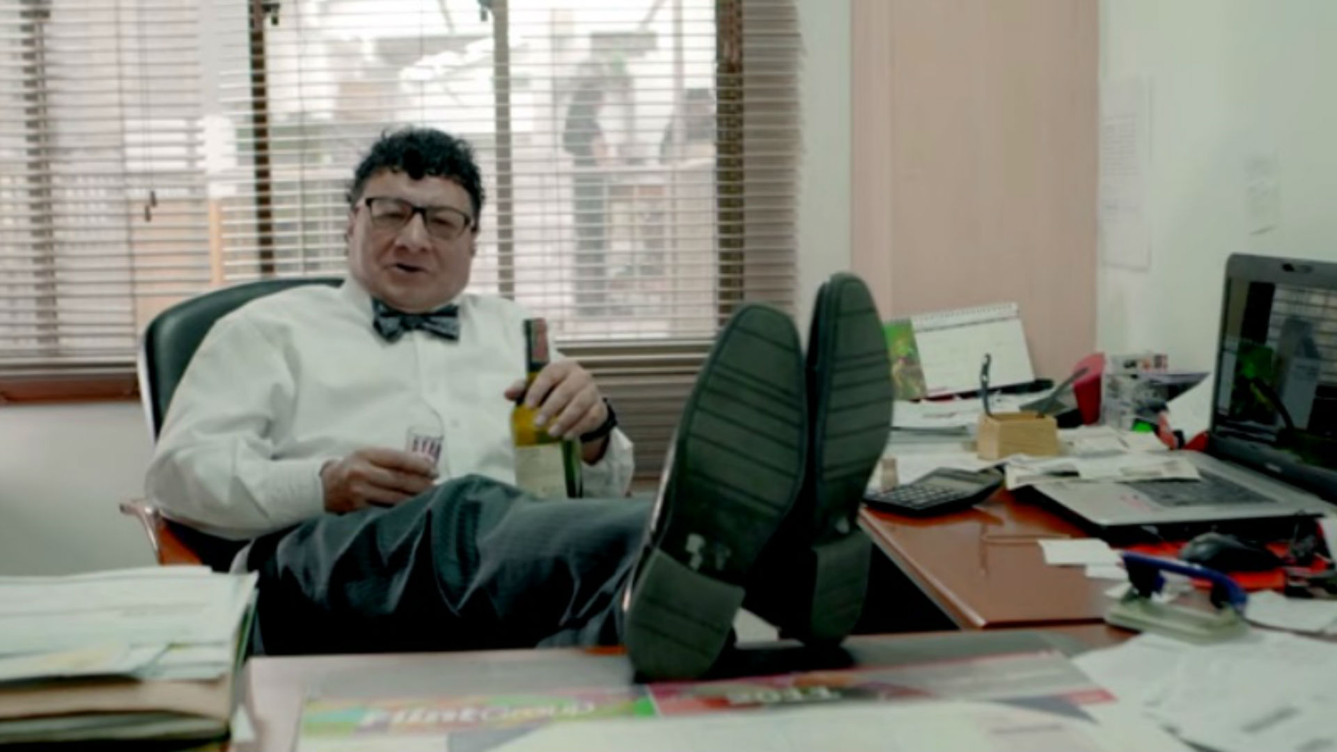 Imagen de Don Devoto sentado en un escritorio con una botella de vino