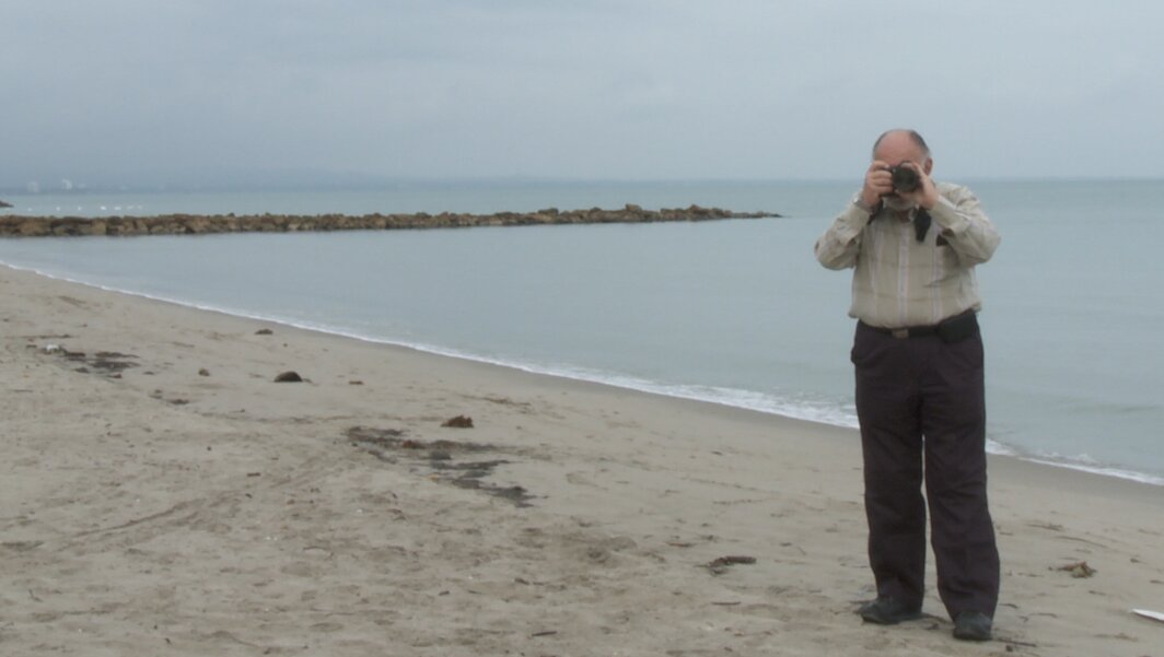 hombre de la tercera edad en la playa tomando una foto