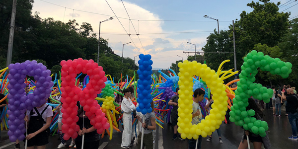 Image of a Pride Parade. Balloon letters spell the word PRIDE in rainbow colours.