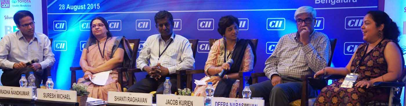 A banner running from left to right of the screen is a picture from a conference. A blue banner is at the background with CII on it. A panel of two men and two women, all seated, is on stage, two of them holding mikes.