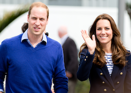 Prince William and Kate Middeton face the camera he is wearing a royal blue sweater and she a navy blazer with gold buttons Kate is waving