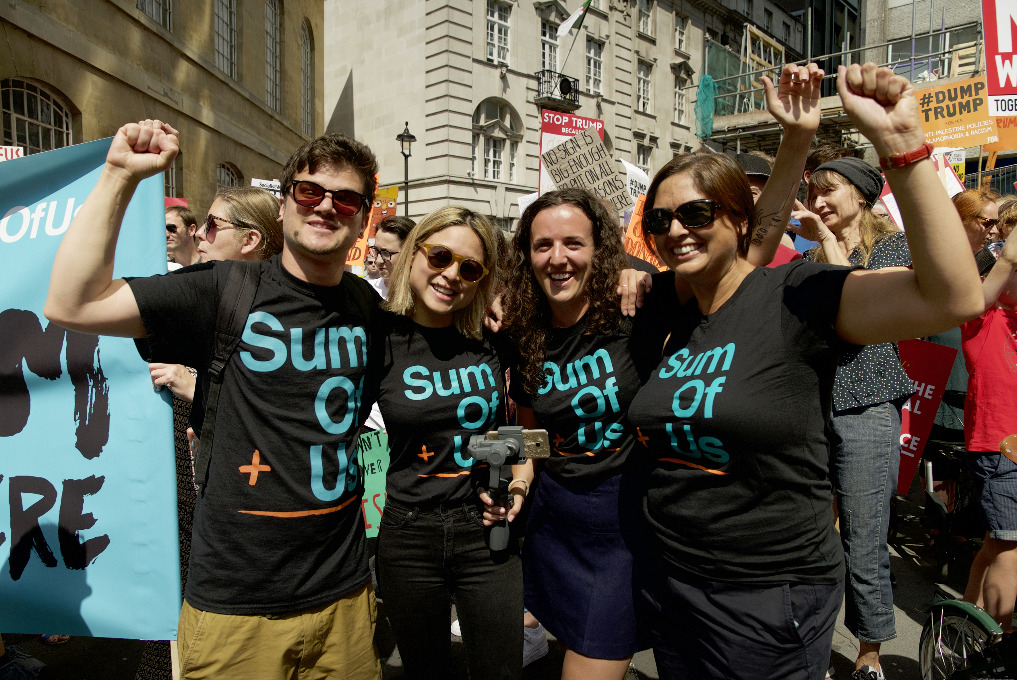 four people wearing sum of us t shirts at a protest