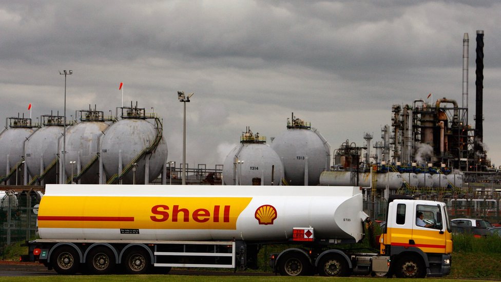 A Shell oil truck passes in front of an oil refinery
