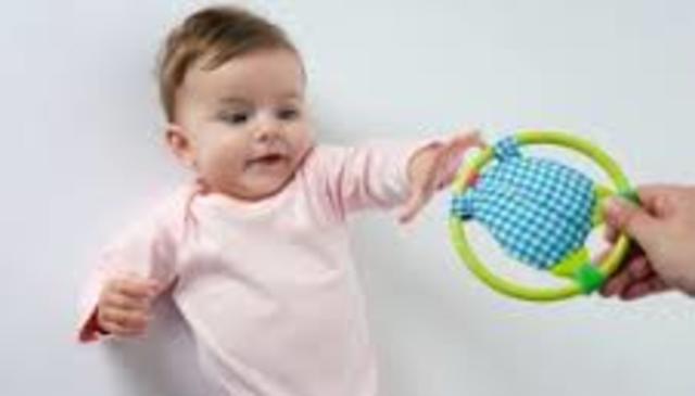 Reaches for toys with one hand