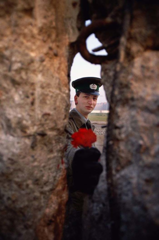 East German soldier passing a flower through the Berlin Wall before it was torn down