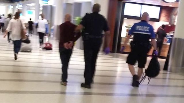 Man is Seen Being Lead Away from the Gate in Handcuffs