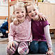 Two smiling little girls best friends sitting on ground in kindergarten e8a9n5