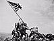 Five Marines and a Navy hospital corpsman raise the flag on Mount Suribachi, Iwo Jima, using a piece of Japanese pipe as a mast.