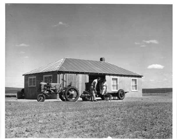 Warren Clifford and wife stand near house with adjoining machine shed on farm