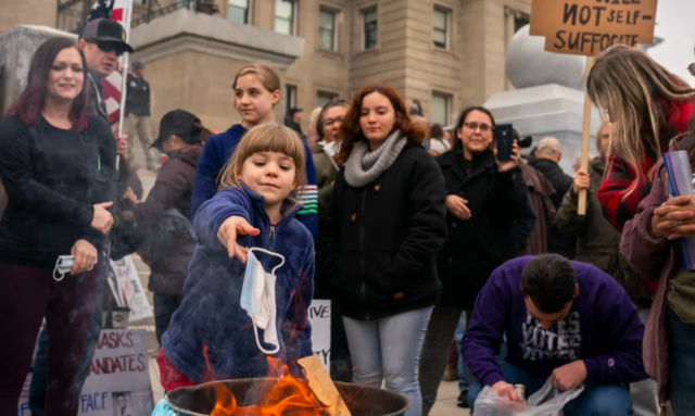 A child puts a mask in a fire during a mask-burning event outside the Idaho Statehouse in Boise. People gathered at at least 20 cities across the state to protest Covid-19 restrictions.