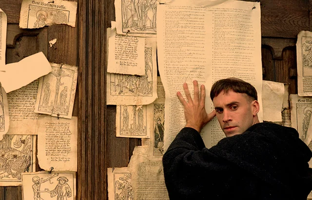 Martin Luther writing the Ninety-Five Theses
