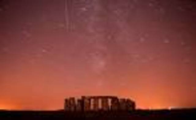 A meteor streaks past stars in the night sky over Stonehenge