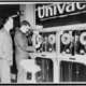 One man looks on as another man prepares univac computer to predict a winning horse