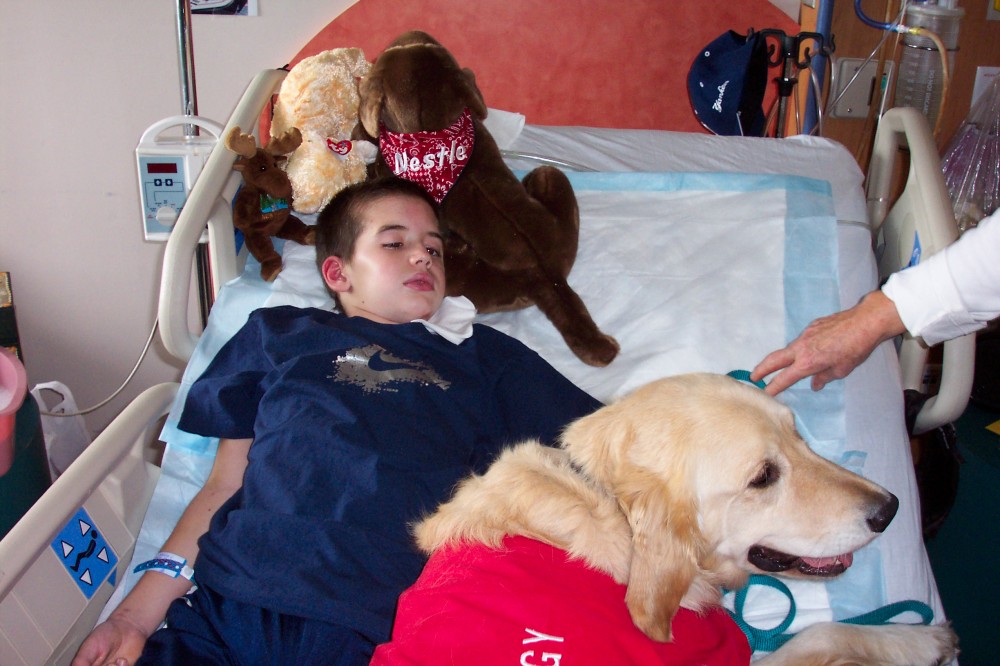 Ryan Boyle in a hospital bed with a therapy dog.