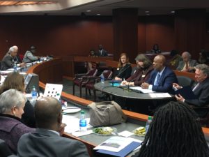 Dwight Robinson at a small table addresses state lawmakers at a large table