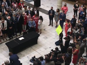 One woman holding a poster kneels at a press conference