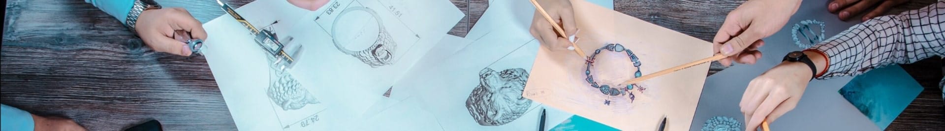 Jewelry designers collaborating over sketches of ring designs on a wooden table.