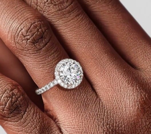 A round halo diamond engagement ring on a hand, showcasing the sparkling center stone surrounded by a halo of smaller diamonds.