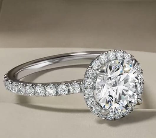 Round-cut diamond halo engagement ring in white gold with pave-set diamonds, showcased on a neutral background.