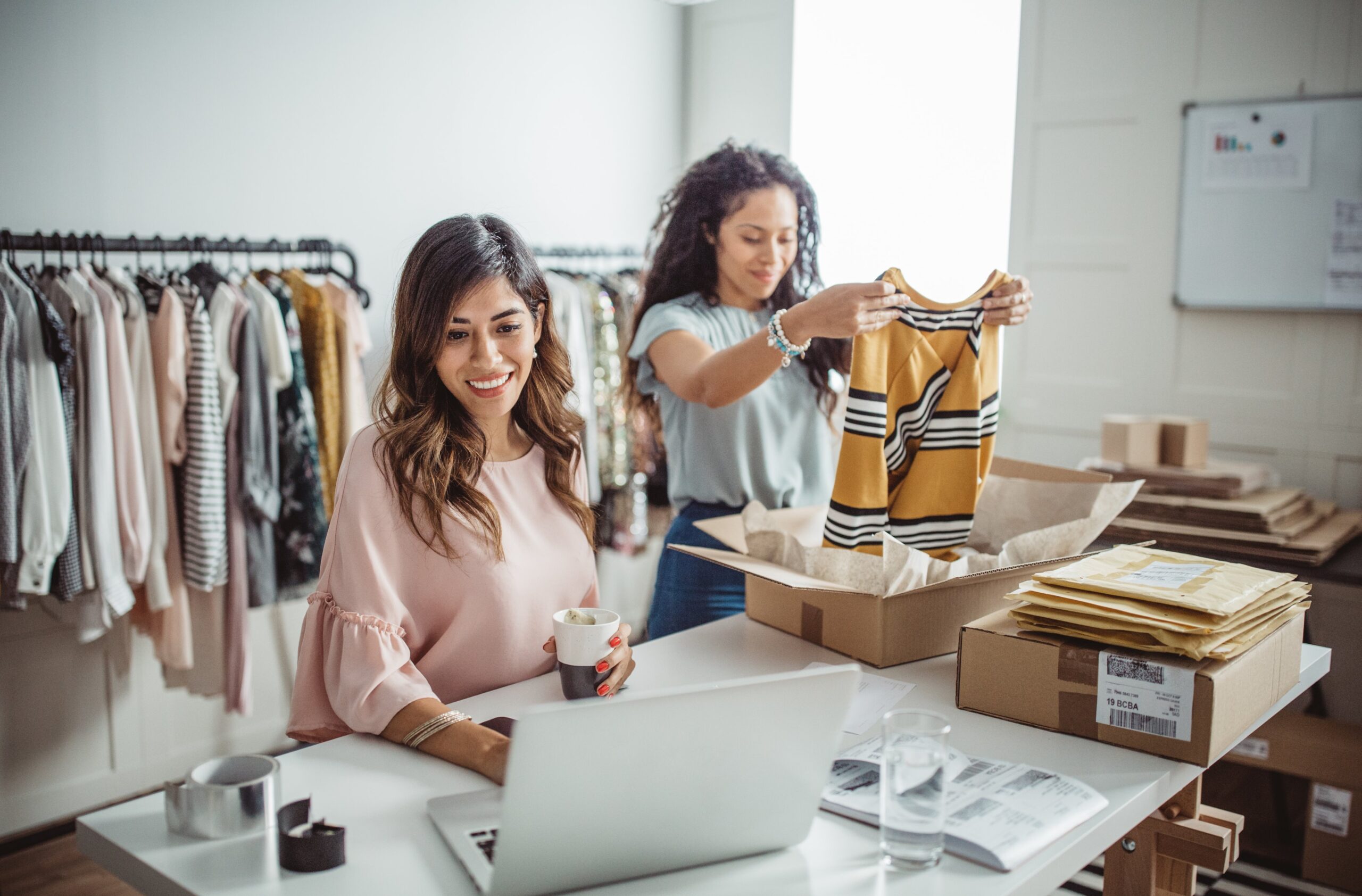Two Hispanic women working on their online clothing store smiling.