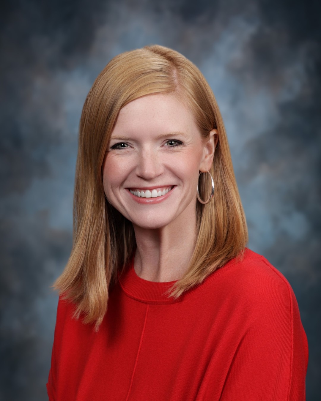 A woman with red hair smiles at the camera, wearing a red top.